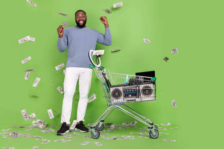 Photo of lucky afro guy wear grey pullover rising fists buying modern devices isolated green color...