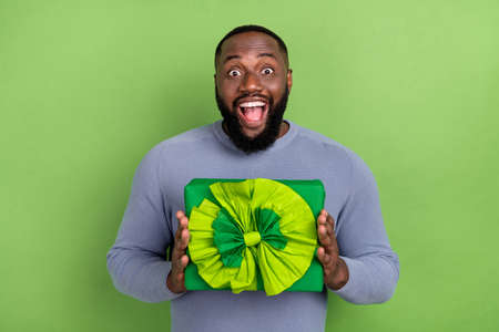 Photo of impressed afro guy wear grey pullover getting present box smiling isolated green color...