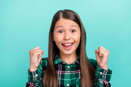Photo of adorable lucky school girl dressed checkered clothes smiling rising fists isolated teal color backgroundの写真素材