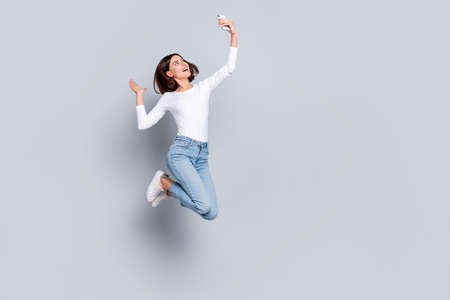 Photo of shiny cute woman wear white outfit jumping high tacking selfie modern device empty space...