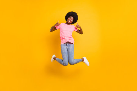 Full size photo of cool millennial lady jump show thumb up wear pink t-shirt jeans isolated on yellow color backgroundの写真素材
