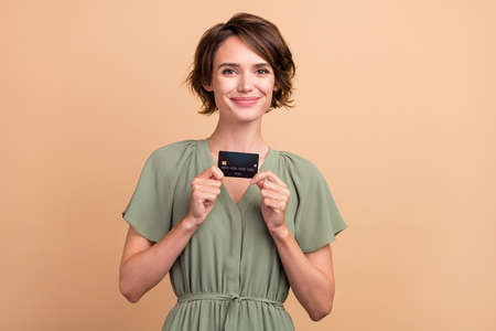 Photo of cheerful pretty lady presenting debit card investment income wear green dress isolated...