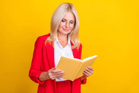 Photo of attractive mature woman read book hobby novel learning isolated over yellow color backgroundの写真素材