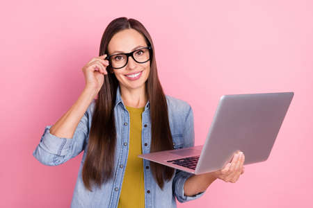 Photo of brunette smart mature lady hold laptop wear eyewear jeans jacket isolated on pastel pink color backgroundの写真素材