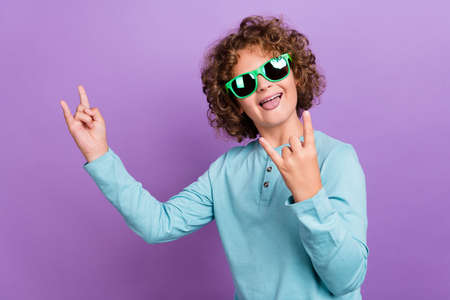 Photo of funny funky schoolboy dressed blue shirt dark glasses showing hard rock signs smiling isolated purple color backgroundの写真素材