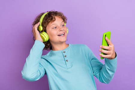 Photo of pretty funny schoolboy dressed blue shirt listening songs typing modern device smiling isolated purple color backgroundの写真素材