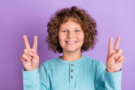 Portrait of attractive cheerful wavy-haired boy showing double v-sign good mood isolated over bright violet purple color backgroundの写真素材