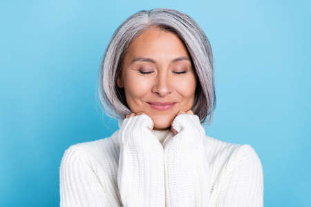 Photo of mature charming asian woman enjoy warmth spring knitwear isolated over blue color backgroundの写真素材