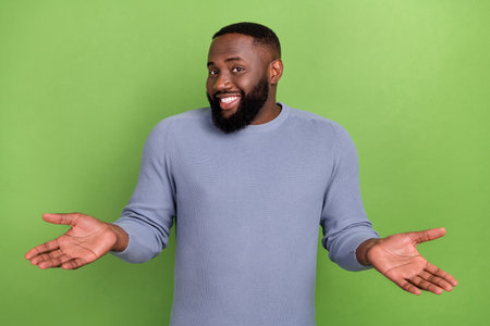 Photo of puzzled afro guy wear grey pullover shrugging shoulders smiling isolated green color backgroundの写真素材