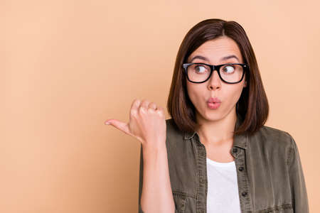 Photo of shocked curious lady indicate thumb empty space look side wear khaki shirt isolated beige...