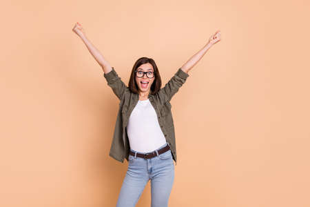 Photo of funny crazy lady raise fists open mouth lucky bet concept wear khaki shirt isolated beige color backgroundの写真素材