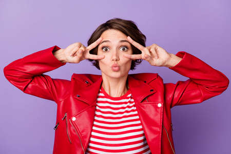 Photo of young attractive woman pouted lips send air kiss show peace cool v-sign isolated over purple color backgroundの写真素材