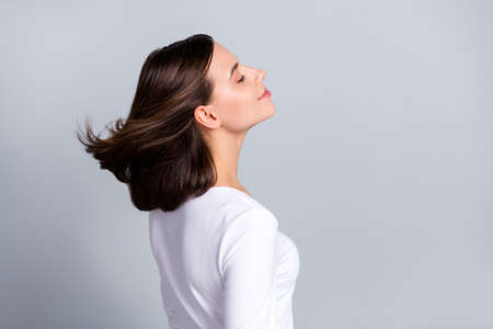 Photo of charming shiny young lady dressed white clothes smiling air blowing empty space closed eyes isolated grey color backgroundの写真素材