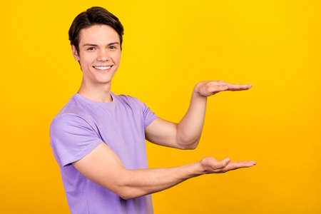 Portrait of attractive cheerful guy demonstrating copy empty blank space invisible thing isolated over bright yellow color backgroundの写真素材