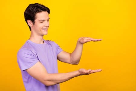 Portrait of attractive cheerful guy holding copy empty blank space place measuring isolated over bright yellow color backgroundの写真素材