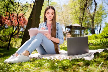 Full body profile side photo of young girl write notebook education study online laptop virtual sit plaid outsideの写真素材