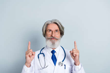 Photo of serious intelligent mature male doctor wear white coat glasses looking pointing up empty space isolated grey color backgroundの写真素材