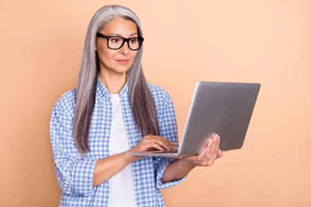 Photo of pretty serious lady pensioner dressed checkered shirt glasses chatting modern gadget isolated beige color backgroundの写真素材