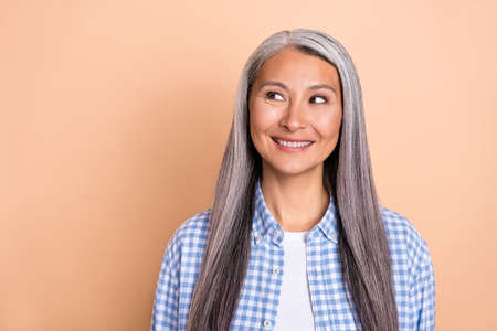 Photo of charming dreamy lady pensioner dressed checkered shirt looking empty space smiling isolated beige color backgroundの写真素材
