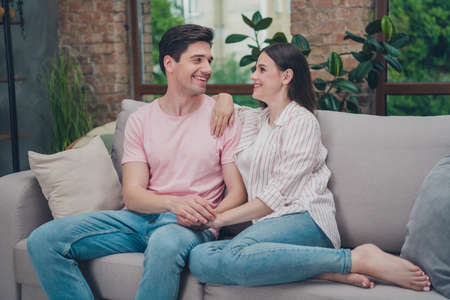 Portrait of attractive careful cheerful spouses sitting on cosy divan homey spending holiday pastime staying at home indoorsの写真素材