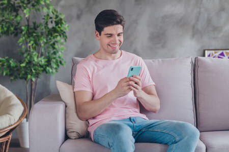 Photo of blogger positive man sit sofa leave comment feedback wear casual outfit in comfortable apartment home indoorsの写真素材