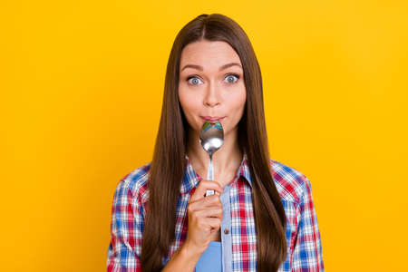Photo of funny cute hungry lady lick silver spoon cutlery advertisement wear plaid shirt isolated yellow color backgroundの写真素材