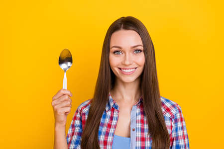 Photo of positive lady hold silver spoon healthy diet promotion wear plaid shirt isolated yellow color backgroundの写真素材