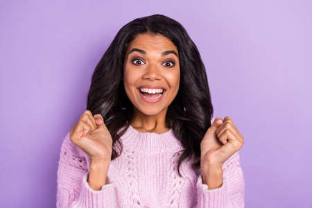 Photo of lucky funny dark skin woman wear pink sweater smiling rising fists isolated violet color backgroundの写真素材