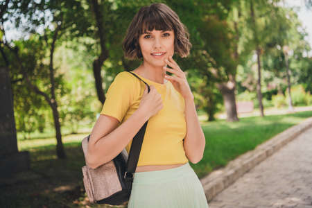Photo of excited charming young lady dressed yellow t-shirt backpack walking smiling outdoors urban parkの写真素材