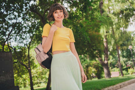 Photo of dreamy adorable young woman wear yellow t-shirt rucksack smiling walking outside city streetの写真素材