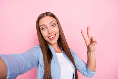 Photo of pretty charming young lady wear casual clothes smiling tacking selfie showing v-sign isolated pink color backgroundの写真素材