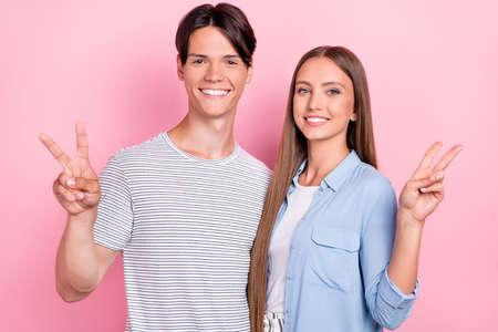 Photo of excited pretty young lovers dressed casual outfits showing v-signs smiling isolated pink...
