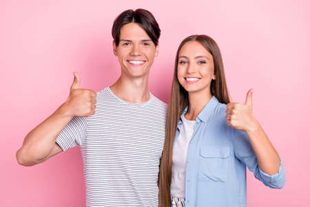 Photo of sweet shiny young couple wear casual clothes smiling embracing showing thumbs up isolated pink color backgroundの写真素材