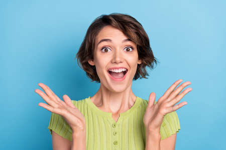 Photo of impressed funky young lady wear green t-shirt smiling rising arms isolated blue color backgroundの写真素材