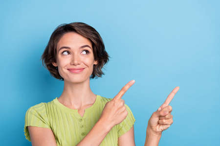 Photo of adorable shiny young woman dressed green t-shirt smiling looking pointing two fingers empty space isolated blue color backgroundの写真素材