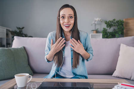 Portrait of attractive amazed cheerful woman sitting on divan using laptop calling web incredible...