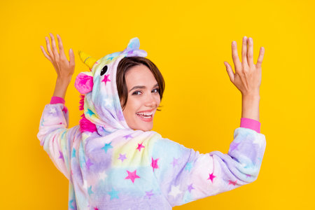 Photo portrait back view woman in unicorn costume smiling in hood isolated bright yellow color backgroundの写真素材