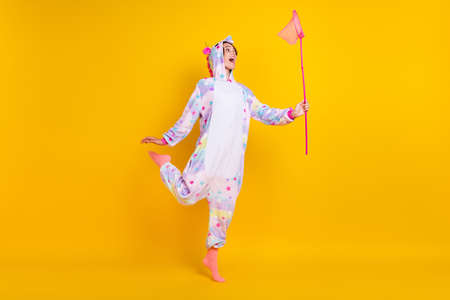 Full length body size photo woman in unicorn costume catching insects with net isolated bright yellow color backgroundの写真素材