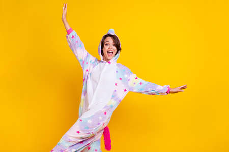 Photo portrait woman in unicorn costume dancing overjoyed on pajama party isolated vibrant yellow color backgroundの写真素材