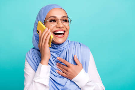 Photo of pretty excited woman wear arab headscarf spectacles talking modern gadget empty space isolated turquoise color backgroundの写真素材