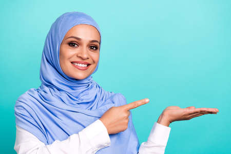 Photo of dreamy cute young lady dressed islamic hijab smiling holding arm pointing empty space...