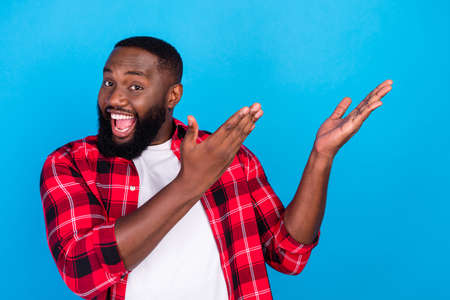 Photo of cheerful happy positive afro american man hold hands empty space show isolated on blue color backgroundの写真素材