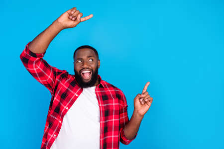 Photo of doubtful happy afro american man point fingers empty space news choose isolated on blue color backgroundの写真素材