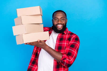 Photo of young happy afro american man hold hands boxes delivery order smile isolated on blue color backgroundの写真素材