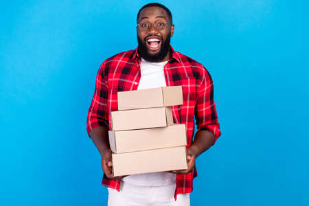 Photo of young happy cheerful man hold hands boxes good mood enjoy isolated on blue color backgroundの写真素材