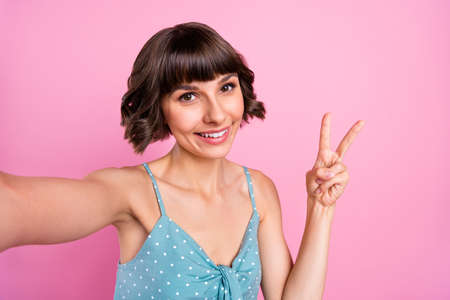 Self-portrait of attractive cheerful girl showing v-sign good mood isolated over pink pastel color backgroundの写真素材