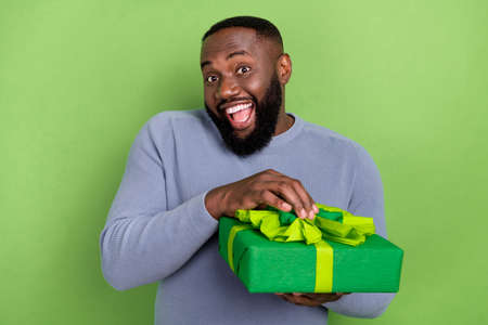 Photo of funny african guy dressed grey sweater smiling opening gift package isolated green color backgroundの写真素材