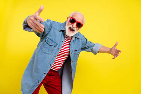 Portrait of attractive cheerful comic childish grey-haired man dancing having fun isolated over bright yellow color backgroundの写真素材