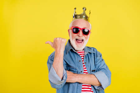 Portrait of elderly retired pensioner trendy handsome grey-haired man in crown copy space isolated over bright yellow color backgroundの写真素材
