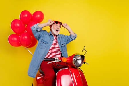 Portrait of elderly retired pensioner trendy man riding moped bargain black friday isolated over vivid yellow color backgroundの写真素材